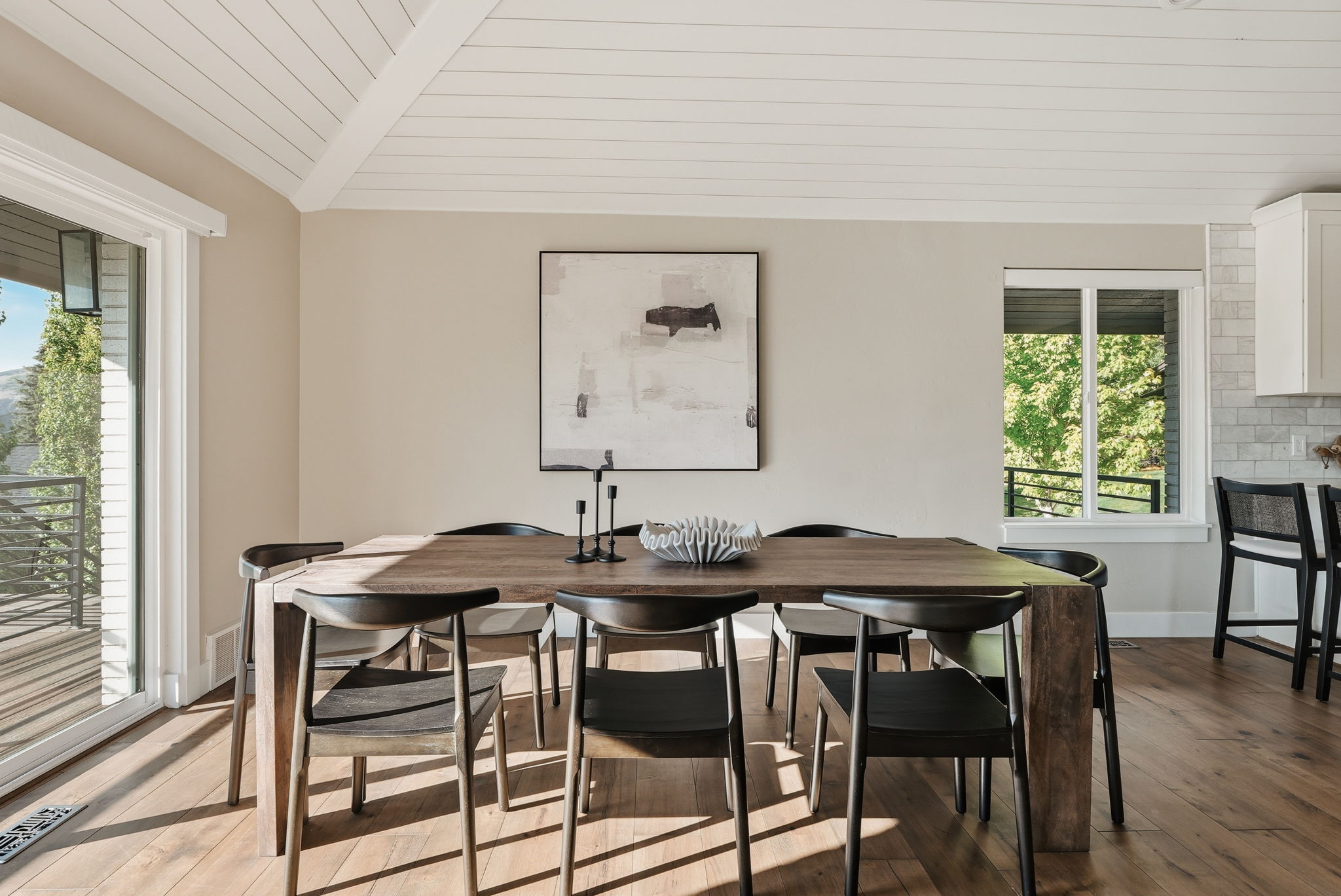 Spacious dining area featuring wood-finish flooring, a vaulted ceiling with white paneling, and an expansive sliding glass door opening to a balcony with metal railings