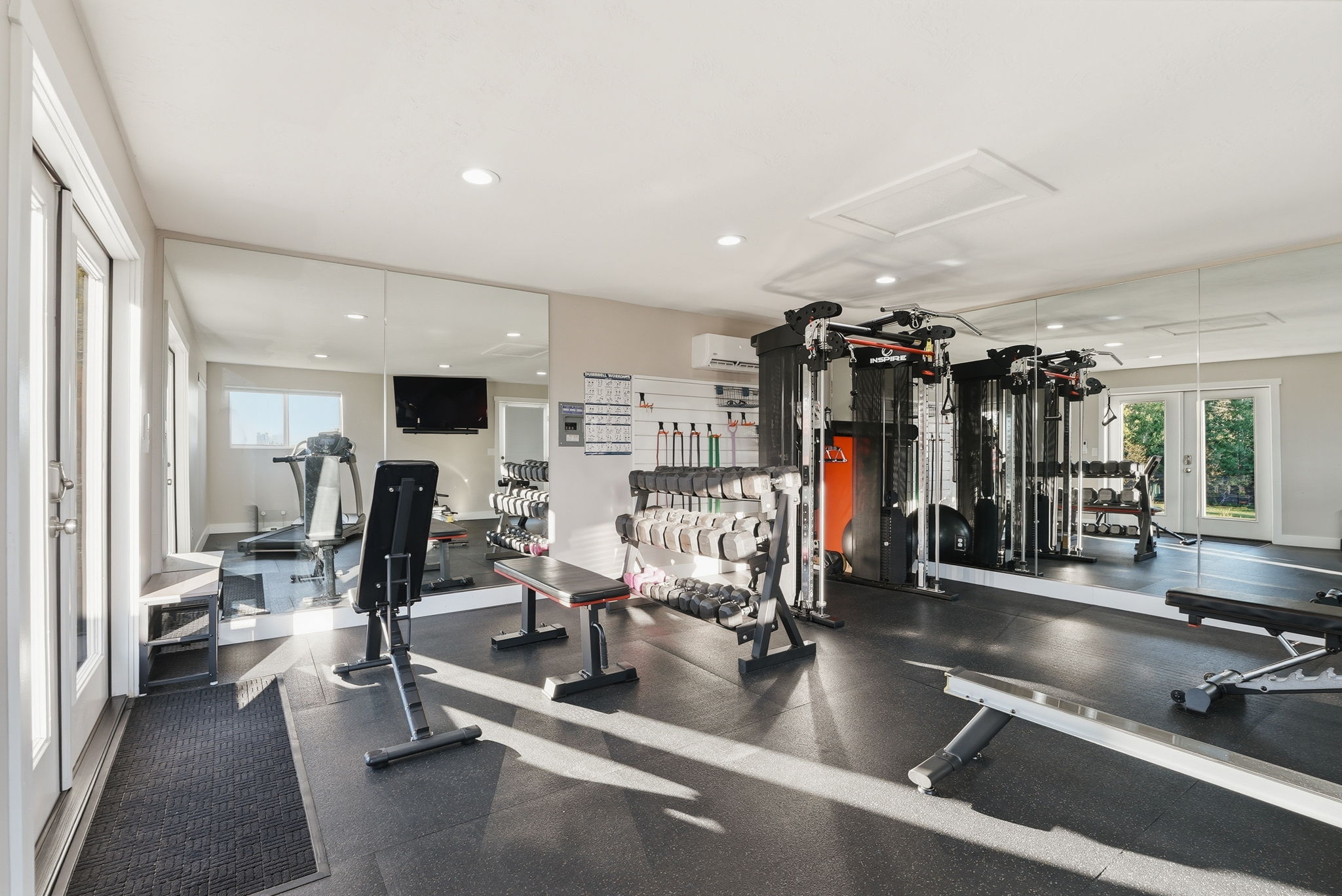 Dedicated fitness room featuring rubberized flooring, mirrored walls, recessed lighting, and white French doors