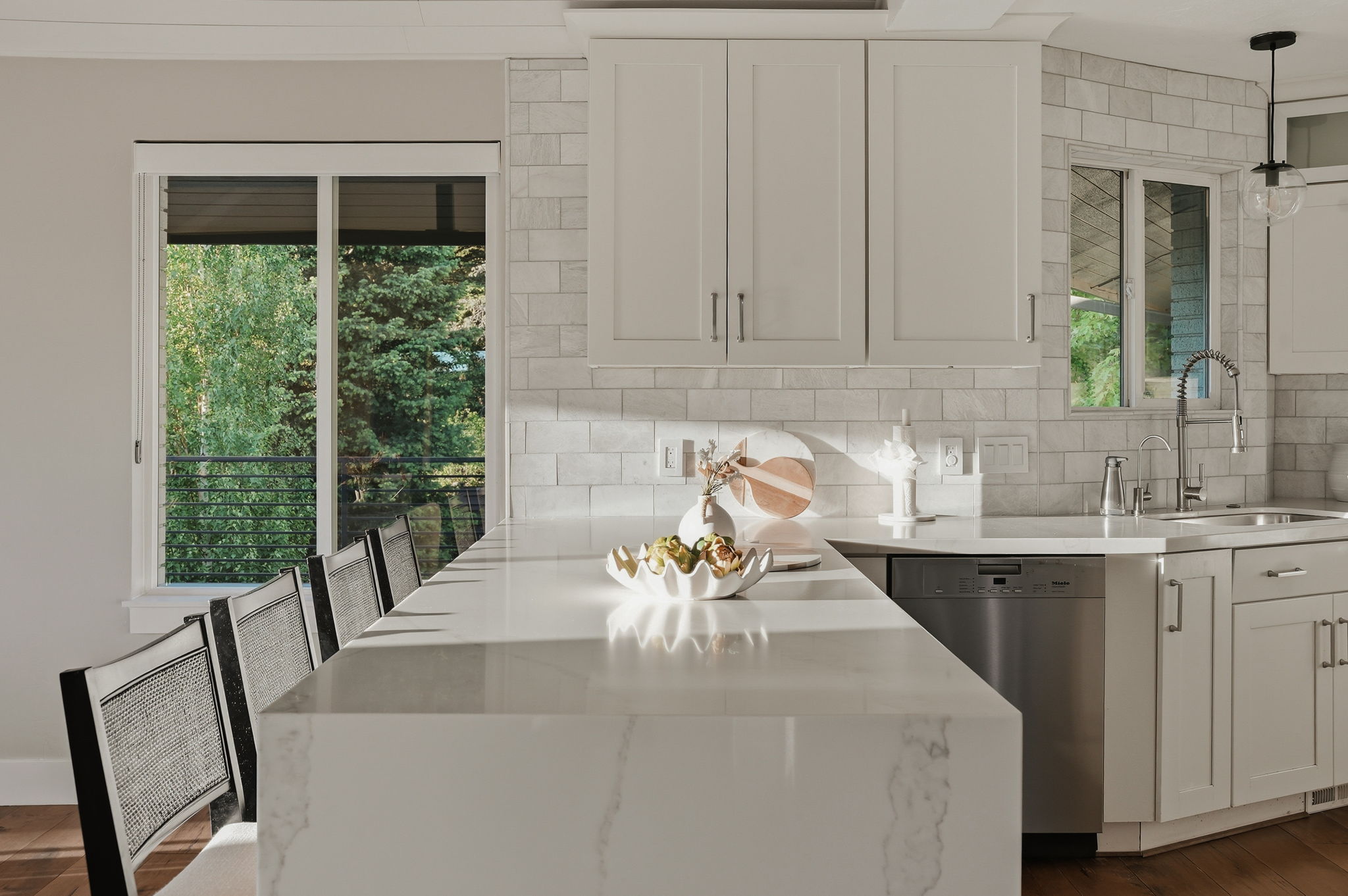 Spacious kitchen featuring a large waterfall-edge island with seating, white shaker cabinetry, a subway tile backsplash, and stainless steel appliances