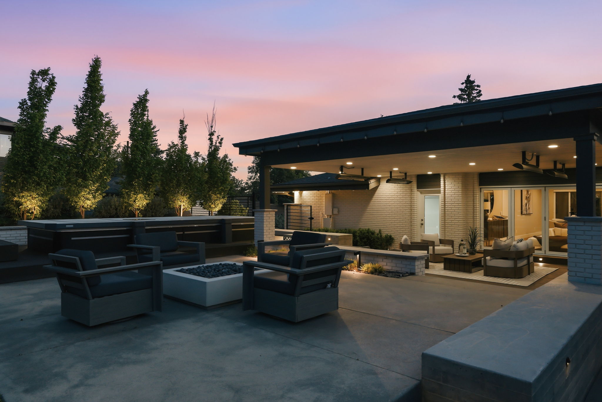 Expansive concrete patio featuring a built-in spa, fire pit, covered outdoor living area with recessed lighting, and integrated planters with uplighting