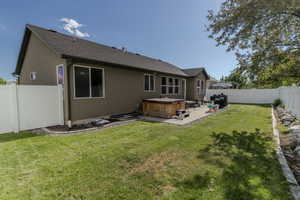 Expansive backyard with a large patio featuring a built-in spa, framed by a white vinyl fence
