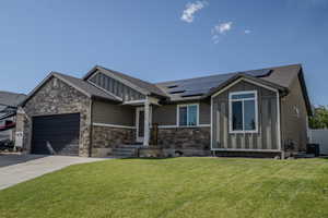 Contemporary residence featuring a stone and siding facade, a dark asphalt shingle roof, solar panels, and a two-car garage