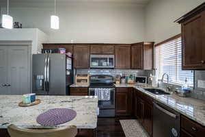 Well-appointed kitchen featuring granite countertops, dark wood cabinetry, stainless steel appliances, a subway tile backsplash, and a large window above the sink