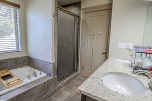 Bathroom featuring a built-in tub, separate shower with frosted glass enclosure, double vanity with stone countertop, and tile flooring