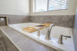 Deep soaking tub with brushed nickel fixtures, surrounded by gray stone-look tile