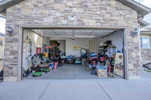 Two-car garage featuring a stone façade, exterior sconce lighting, and a concrete driveway