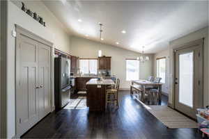 Open-concept kitchen and dining area featuring dark wood-finish flooring, vaulted ceilings with recessed lighting, and a kitchen island with seating