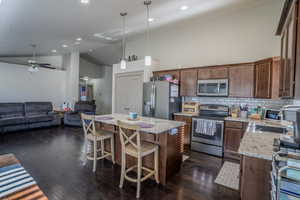 Open-concept kitchen and living area featuring dark wood-finish flooring, vaulted ceilings, and recessed lighting