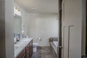 Bathroom featuring a dual vanity with light-toned countertops and wood-finish cabinetry, a commode, a built-in bathtub with tiled surround, and tiled flooring