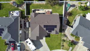 Aerial view featuring a residential property with a brown shingle roof and integrated solar panels