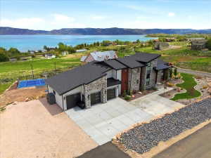 Modern multi-level residence featuring stone and wood-paneled accents, multiple garage bays, a paved driveway, and a backyard sports court