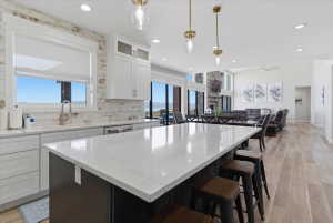 Open-concept living area featuring a kitchen island with seating, white shaker-style cabinetry, a white brick backsplash, and a stainless steel sink with a gooseneck faucet