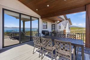 Expansive covered patio featuring a wood-finish ceiling with recessed lighting, composite decking, and metal railings