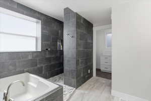 Spacious bathroom featuring a white soaking tub with brushed nickel fixtures, dark gray stone-look wall tiling, an open shower with a tiled floor, and light wood-look floor tiling