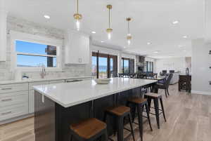 Kitchen featuring a substantial island with a white countertop and seating, brass pendant lighting, white cabinetry, and a stacked stone backsplash