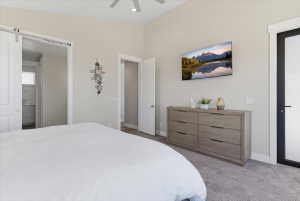 Spacious bedroom featuring light neutral wall paint, gray carpeting, a built-in ceiling fan, and a white barn door leading to an en-suite bathroom with a vanity and window