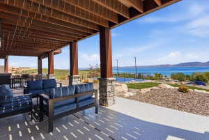 Expansive covered patio featuring a wood-beam ceiling, stone-clad columns, and a speckled concrete floor