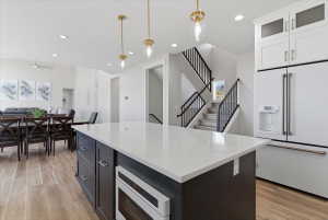 Open concept living area featuring a large kitchen island with a light-toned countertop, wood-finish flooring, recessed lighting, and a contemporary staircase with black railings
