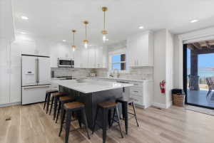 Modern kitchen featuring white cabinetry, a large center island with seating, stainless steel appliances, and wood-finish flooring