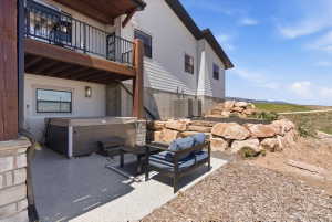 Lower-level patio featuring a hot tub, rock landscaping, and an upper deck with black metal railings