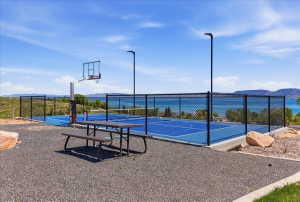 Outdoor recreational area featuring a full-size basketball hoop, fenced court with blue surfacing, and a picnic table