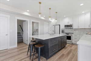 Contemporary kitchen featuring a dark-toned island with integrated storage, white perimeter cabinetry, stainless steel appliances, and wood-finish flooring