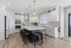 Gourmet kitchen featuring a large central island with seating, wood-finish flooring, white cabinetry, integrated stainless steel appliances, and a tiled backsplash