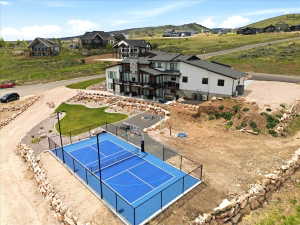 Expansive exterior featuring a dedicated sport court with a fence enclosure, multi-level patio spaces, mature landscaping, and a substantial retaining wall