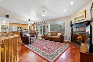 Open-concept living space featuring wood-finish flooring, a fireplace with a black wood mantel, vaulted ceilings, and recessed lighting