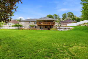 Spacious green lawn with a two-story brick exterior featuring a covered upper deck with wood railing and a lower patio with French doors