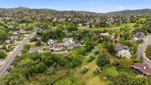 Expansive aerial view showcasing the property within a verdant, hilly residential area, featuring surrounding mature trees and distant mountain ranges