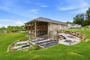 Expansive terraced backyard featuring a brick exterior, upper-level wood deck, lower-level covered patio, and multiple raised garden beds