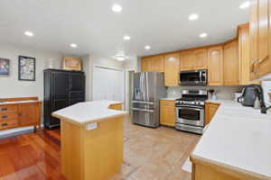 Kitchen featuring light wood cabinetry, stainless steel appliances, a center island with a light countertop, and a mix of tile and wood-finish flooring