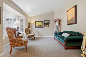 Sunken living room featuring plush carpet flooring, a bay window with plantation shutters, an angled ceiling, and neutral-toned wall paint