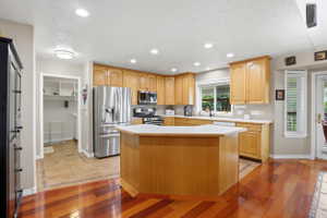 Kitchen featuring a central island with countertop, light wood cabinetry, recessed lighting, stainless steel appliances, and a combination of wood-finish and tile flooring