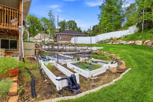 Terraced backyard featuring multiple raised garden beds, a manicured lawn area, and a white privacy fence