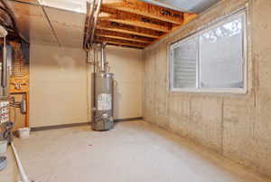 Unfinished basement space featuring exposed ceiling joists, concrete flooring, and a single window