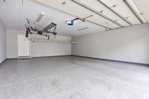 Spacious garage featuring a speckled epoxy floor coating, light grey painted walls, and overhead fluorescent lighting