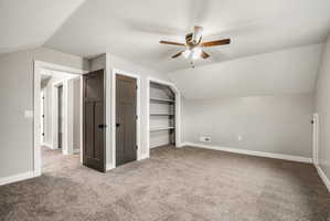 Carpeted room with sloped ceiling, dark wood-finish interior doors, recessed shelving, and a ceiling fan