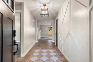Entryway featuring a patterned tile floor, decorative wall paneling, a contemporary ceiling light fixture, and an open doorway revealing a carpeted room