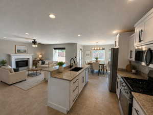 AI Rendering to help you vision it with your furniture. Open-concept living space featuring a central kitchen island with a dark sink and matte black faucet, light-toned granite countertops, stainless steel appliances, and white cabinetry with dark hardwa