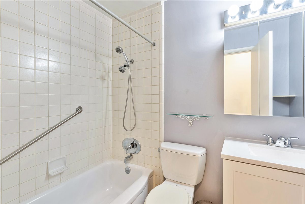 Bathroom featuring a white tiled shower with a chrome shower head and grab bar