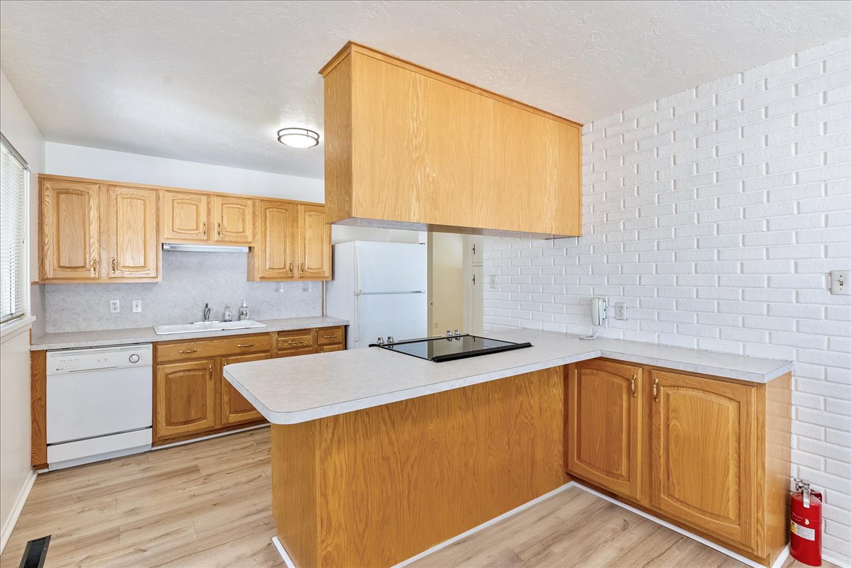 Kitchen featuring light wood cabinetry, laminate countertops, a white dishwasher, and a built-in cooktop