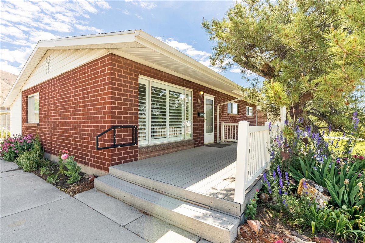 Brick exterior with a large front window featuring internal blinds, complemented by a composite decking porch with white railing