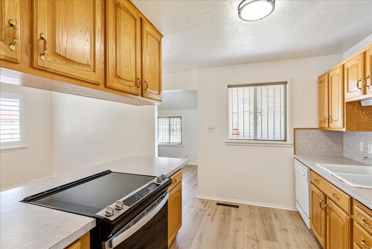 Kitchen featuring wood cabinetry, light-toned countertops, a built-in electric range, and wood-finish flooring