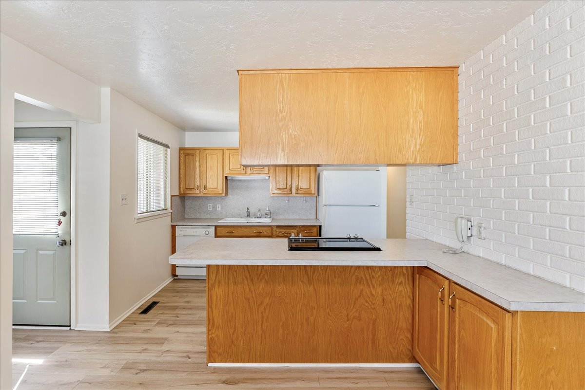 Kitchen featuring light wood cabinetry, a built-in cooktop, and a white brick-patterned accent wall
