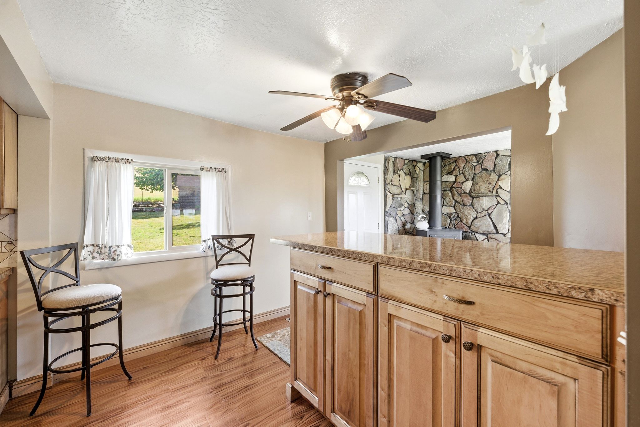 Open kitchen area featuring wood-finish flooring, a ceiling fan, and a pass-through to a stone accent wall with a wood-burning stove
