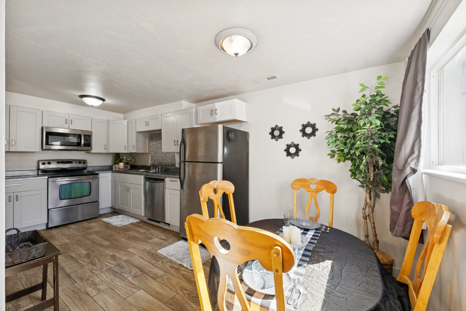 Kitchen and dining area featuring wood-finish flooring, white cabinetry, stainless steel appliances, and a window