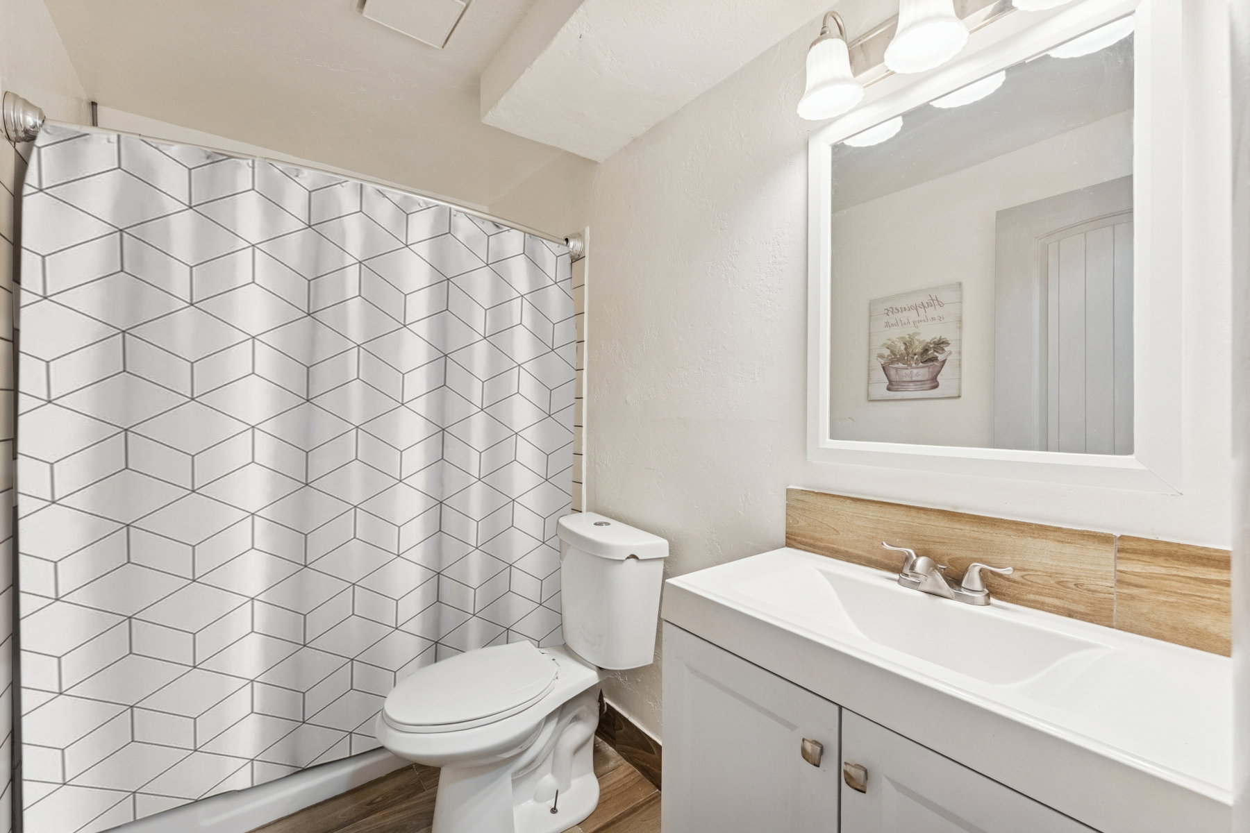 Bathroom featuring a single vanity with an integrated sink, a rectangular mirror, a three-light vanity fixture, and wood-finish flooring
