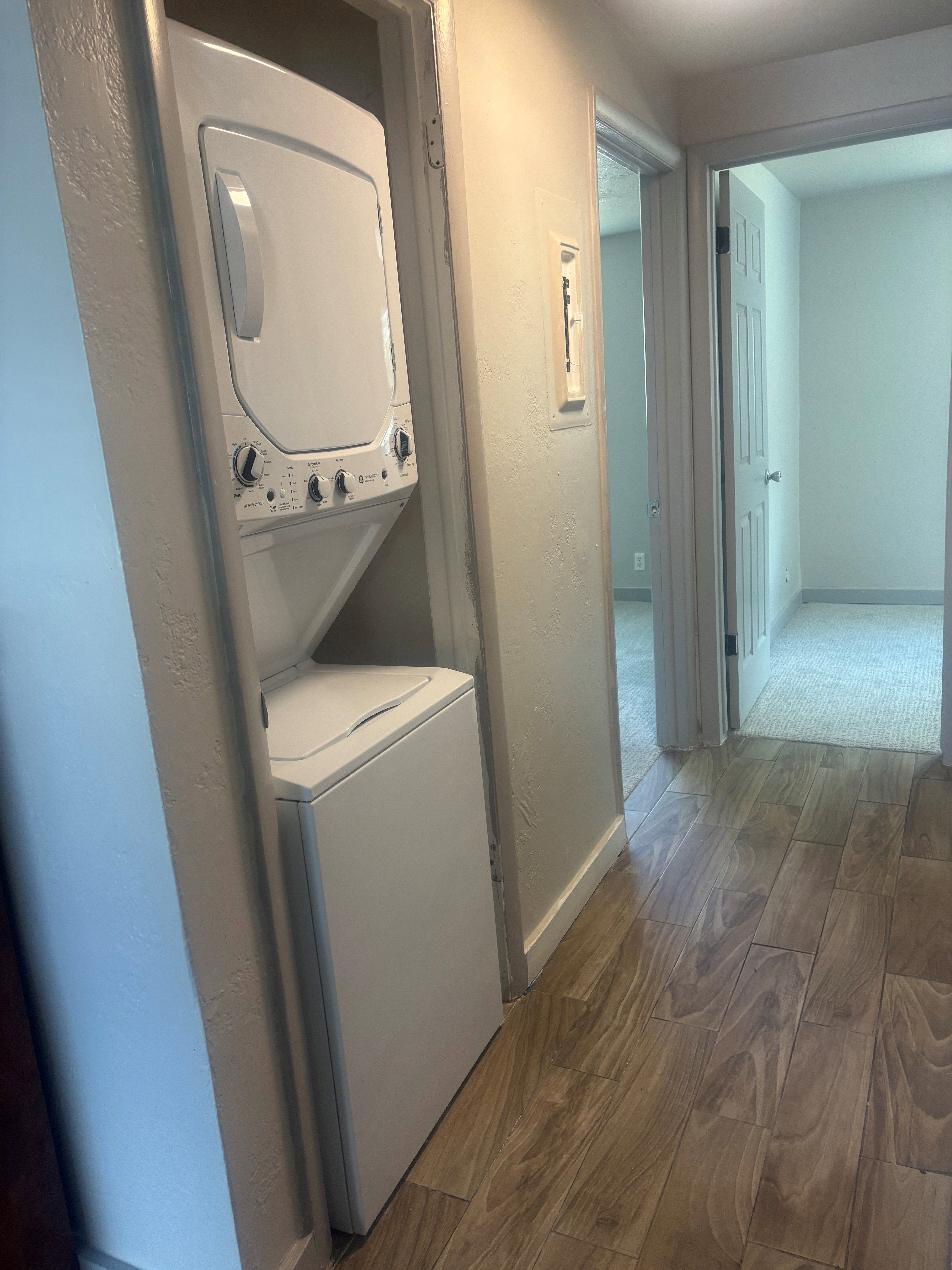 Dedicated laundry closet featuring a white stacked washer and dryer unit, complemented by wood-finish flooring